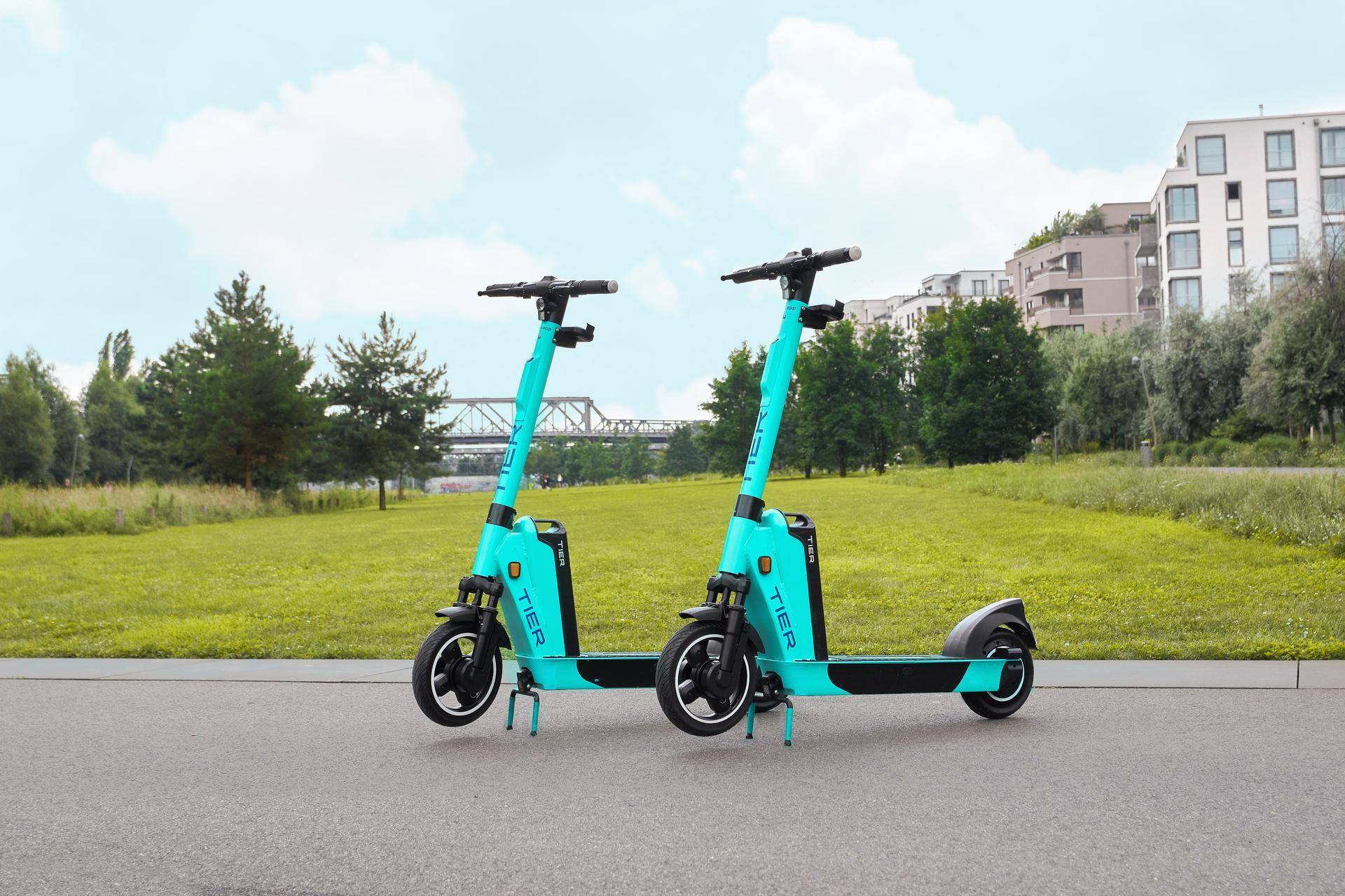 A photo of two Tier E-Scooters near a green field.